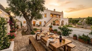 Cortile di una Masseria pugliese al tramonto, con mura in pietra bianca e un ulivo secolare, illuminato da una luce dorata.
